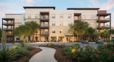exterior of a multi-story building with a walkway featuring lush landscaping