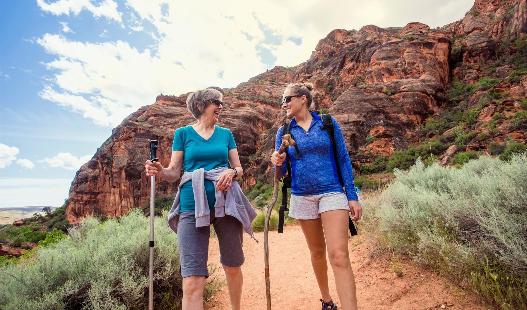 a couple of women walking on a trail with a mountain in the background